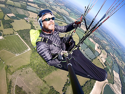 shot of man paragliding or hang gliding from side over rolling fields.